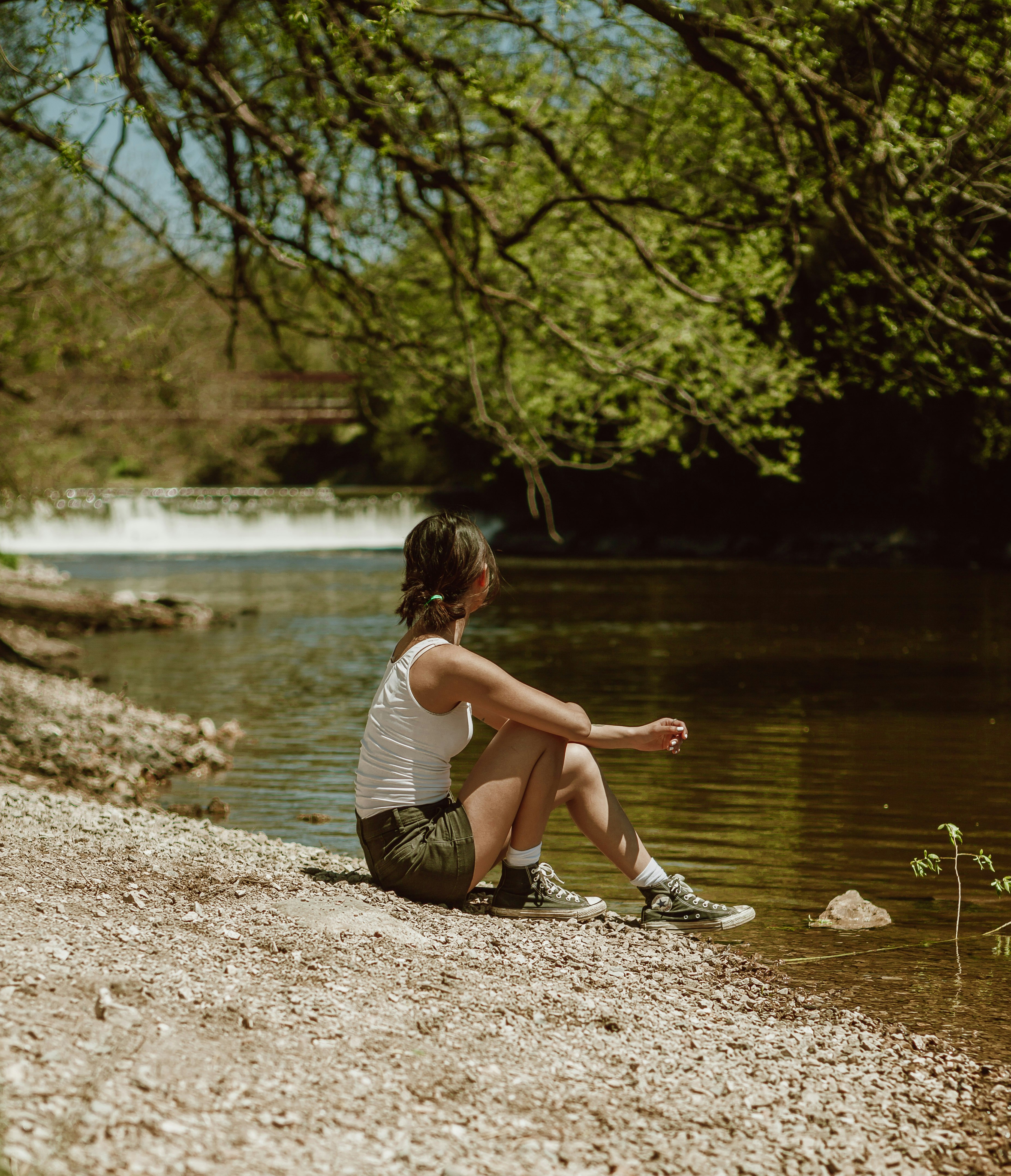 girl in white and black stripe tank top sitting on brown soil near river during daytime